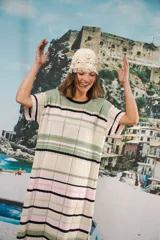 Vestido largo de tejido calado con rayas horizontales en tonos beige, marrón y amarillo. Tiene corte recto, hombros caídos, tajo lateral y logo bordado en la manga.