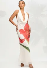 Vestido largo de fiesta color blanco con estampado floral de amapolas rojas. Presenta un escote halter con cuello drapeado, espalda descubierta y una silueta fluida y elegante.