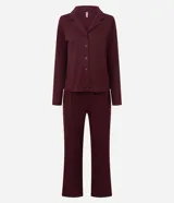 Pijama largo de dos piezas marca Lov, confeccionado en tejido rib de poliéster con elastano. La blusa es de manga larga estilo americano con cuello solapa y cierre frontal de botones. El pantalón es de corte recto con cintura satinada.