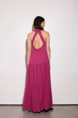 Vestido largo fucsia con escote halter y espalda baja. Tiene volado en el cuello y maxi volado en la cadera.