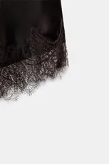 Top lencero de tejido satinado color marrón oscuro, con escote en V y tirantes finos ajustables. El bajo es asimétrico y está adornado con encaje a tono.