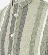 Camisa de hombre de manga corta con cuello tradicional y abotonado frontal. Presenta un tejido texturizado con un patrón de rayas verticales en tonos beige, blanco y marrón claro.