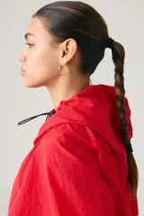 Campera parka roja estilo blouson con capucha ajustable, cierre frontal de botones a presión, bolsillos frontales con solapa y diseño holgado.