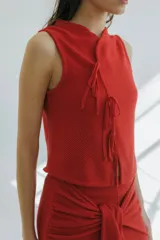 Top tejido en punto arroz color beige, de corte recto y sin mangas, con detalle frontal de lazos finitos decorativos.