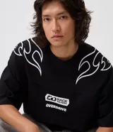 Remera oversized de color negro, confeccionada en algodón con cuello redondo y manga corta. Presenta estampados de llamas de estilo maorí en los hombros y gráficos de lettering en el pecho con las inscripciones "Race Team" y "Overdrive".