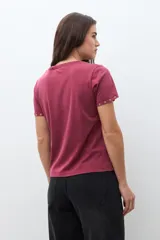 Remera de algodón color bordó, con cuello redondo, manga corta y detalle de ojalillos metálicos en el borde de las mangas.
