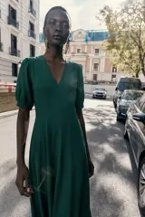 Vestido midi de color marrón chocolate, con escote en pico y mangas cortas abullonadas con puños elásticos. Presenta costuras verticales decorativas en el frente y cierre de cremallera oculta en la espalda.