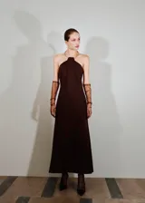 Vestido largo color marrón, diseño evasé y sin mangas, con cuello halter integrado a un cuello rígido metálico tipo choker.