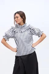 Blusa a rayas verticales en color negro y blanco, con cuello alto fruncido y volados. Mangas cortas abullonadas con puños elastizados con volados.