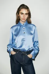 Camisa de cuello solapa y manga larga, confeccionada en tejido satinado con acabado brillante. Presenta cierre frontal con botones y bajo asimétrico.