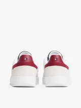 Zapatillas urbanas de corte bajo con exterior de ante blanco, detalles en gris y azul celeste, y refuerzo en el talón de cuero burdeos. Presentan el logo de la marca bordado en el lateral y en la parte trasera.