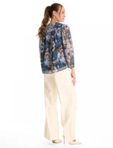 Blusa de gasa con estampado floral en tonos azules y marrones, con sutiles hilos de lurex dorados. Presenta cuello a la base, abertura central con botones, canesú delantero con pasamanería calada y mangas largas con puños elastizados. Incluye forro interno a tono.