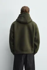 Sudadera de corte relajado confeccionada en tejido técnico con elasticidad y efecto neopreno. Presenta capucha ajustable con cordones, cierre frontal de cremallera de doble dirección, bolsillos tipo canguro y terminaciones en rib.