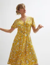 Vestido midi cruzado de color ocre con diseño floral estampado, escote en V y mangas cortas con vuelo. Cuenta con un lazo ajustable en la cintura.