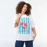 Camiseta blanca de corte oversize y manga corta con diseño estampado de rayas verticales celestes, tomates y la inscripción 'Tomato Club'.
