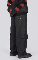 Pantalón cargo oversize de microfibra pesada en color negro, con silueta estructurada, bolsillos laterales de gran tamaño con solapa y broches snap, cintura elástica con cordón de ajuste y cierre frontal.