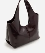 Cartera shopper grande Satinato confeccionada en PU color bordó con acabado efecto charol, diseño amplio de trapecio invertido, asas amplias para el hombro y cierre magnético.
