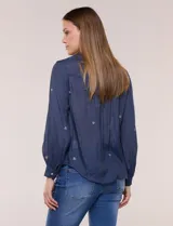 Camisa de estilo boho, color verde, con cuello camisero, escote en V y botonadura frontal con botones perlados. Cuenta con una pechera con bordados geométricos y florales a contraste, mangas largas abullonadas con puños abotonados y delicados bordados dispersos.