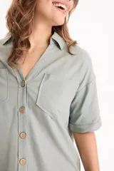 Camisa de lino color beige, de manga corta, con cuello camisero, bolsillos delanteros con solapa y cierre frontal con botones de madera.