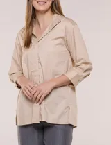 Camisa de silueta holgada y largo extendido, confeccionada en poplín elástico de color blanco. Presenta cuello solapa abierto en V con cartera frontal de abotonadura oculta, hombros caídos y mangas tres cuartos. Cuenta con espalda con canesú, pliegue central y ruedo recto con pequeñas aberturas laterales.