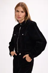 Chaqueta corta de terciopelo negro con efecto desgastado en tono azulado, cuello mao, cierre frontal metálico y bolsillos frontales con tapa y botón.