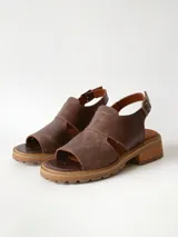 Sandalias de cuero color chocolate con suela track y taco bajo cuadrado. Poseen capellada cerrada con aberturas laterales y tira ajustable en el talón con hebilla metálica.