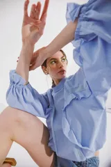 Blusa celeste de cuello alto y manga larga con elástico en el puño. Presenta detalles de volados en el frente y en los puños.