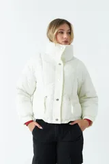 Campera puffer cropped color blanco, de corte a la cintura, con cuello alto, cierre metálico frontal con botones a presión y bolsillos laterales con cierre invisible.