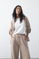 Pantalón de corte holgado y pierna ancha, con cintura elástica ajustable mediante cordón. Presenta bolsillos laterales y costuras verticales decorativas que recorren el frente de las piernas.