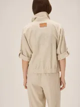 Chaquetas de lino bicolor en tonos blanco y beige, con diseño holgado, cuello alto, cierre frontal de botones, bolsillos con solapa en el pecho y mangas cortas con presilla y botón.