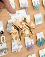 Aros colgantes dorados con forma geométrica irregular y textura arrugada.