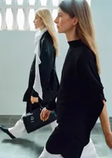 Vestido corto negro de corte recto con cuello alto y mangas asimétricas. Cuenta con cierre posterior de cremallera y botones.