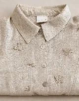 Camisa de lino 100% natural color beige, con cuello camisero, cierre frontal con botones de nácar y delicados bordados florales hechos a mano.