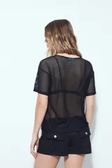 Top de manga corta de tejido mesh (tipo red) color verde militar, con calce relajado y nudo frontal. Se sugiere usar sobre otra prenda debido a su transparencia.