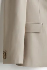 Blazer slim fit de botonadura sencilla en color beige, con solapas de muesca, bolsillos con solapa y cierre de botones.