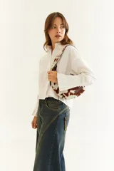 Camisa de corte boxy en color blanco, con cuello clásico, cierre frontal de botones y mangas largas con puños estructurados con tablas. Presenta costuras a contratono y detalle de frunce en la espalda.