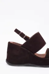 Sandalias de cuero vacuno color negro, con taco de cuña y tira ancha sobre el empeine. Ajuste con hebilla al tobillo.