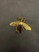 Dije con forma de abeja en metal dorado, con alas detalladas y cuerpo decorado con pequeñas piedras naturales facetadas en tonos variados.