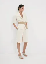 Blazer corto de mezcla de lino en color beige con rayas sutiles, de corte recto, cuello con solapa de muesca, mangas tres cuartos, cierre frontal de un botón y bolsillos con solapa.