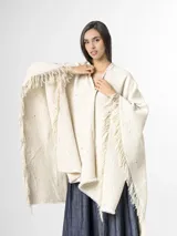 Ruana off white de tejido texturado con detalles sutiles de hilos multicolor y terminación de flecos en los bordes.