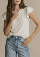 Remera color blanco tiza, de corte recto y cuello redondo. Presenta mangas cortas con volados superpuestos de tela con bordados calados (ojales).