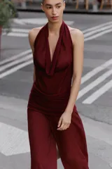 Mono largo de punto color bordó, con escote halter drapeado, hombros descubiertos y detalle de fajín fruncido en la cintura.
