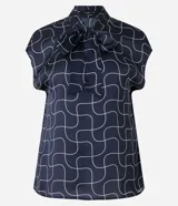 Blusa azul marino con estampado de líneas geométricas blancas, cuello alto con lazo y mangas cortas.