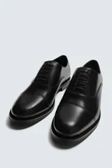 Zapato de vestir tipo oxford con puntera reforzada, confeccionado en piel lisa de color negro. Presenta cierre de cordones, forro interior y plantilla de piel, y suela con tacón bajo.