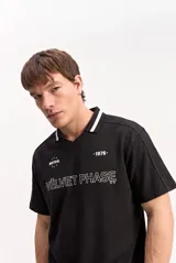 Remera polo de manga corta con textura, color negro, cuello en V con solapa y detalles en contraste blanco. Presenta estampas frontales de inspiración deportiva y urbana.