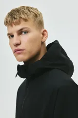 Campera rompevientos negra de nylon repelente al agua, con capucha ajustable, cierre frontal, bolsillos laterales y puños elásticos.