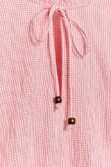 Blusa de manga larga con estampado de cuadros vichy en tonos rosado y blanco. Presenta cuello redondo con volante, cordón ajustable en el escote con apliques decorativos, y puños fruncidos con tiras para atar.