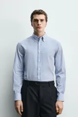 Camisa regular fit de algodón con diseño de rayas finas celestes y blancas. Cuenta con cuello abotonado, manga larga con puños abotonados y cierre frontal de botones.