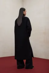 Abrigo largo de lana reciclada en color negro, con cuello redondo, cierre frontal con botones ocultos, bolsillos laterales y aberturas en los costados.