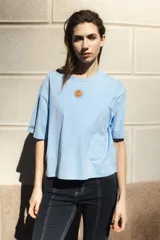 Remera celeste de algodón con cuello redondo y mangas cortas. Presenta un bordado pequeño de un sol en el pecho y rayas horizontales en las mangas.